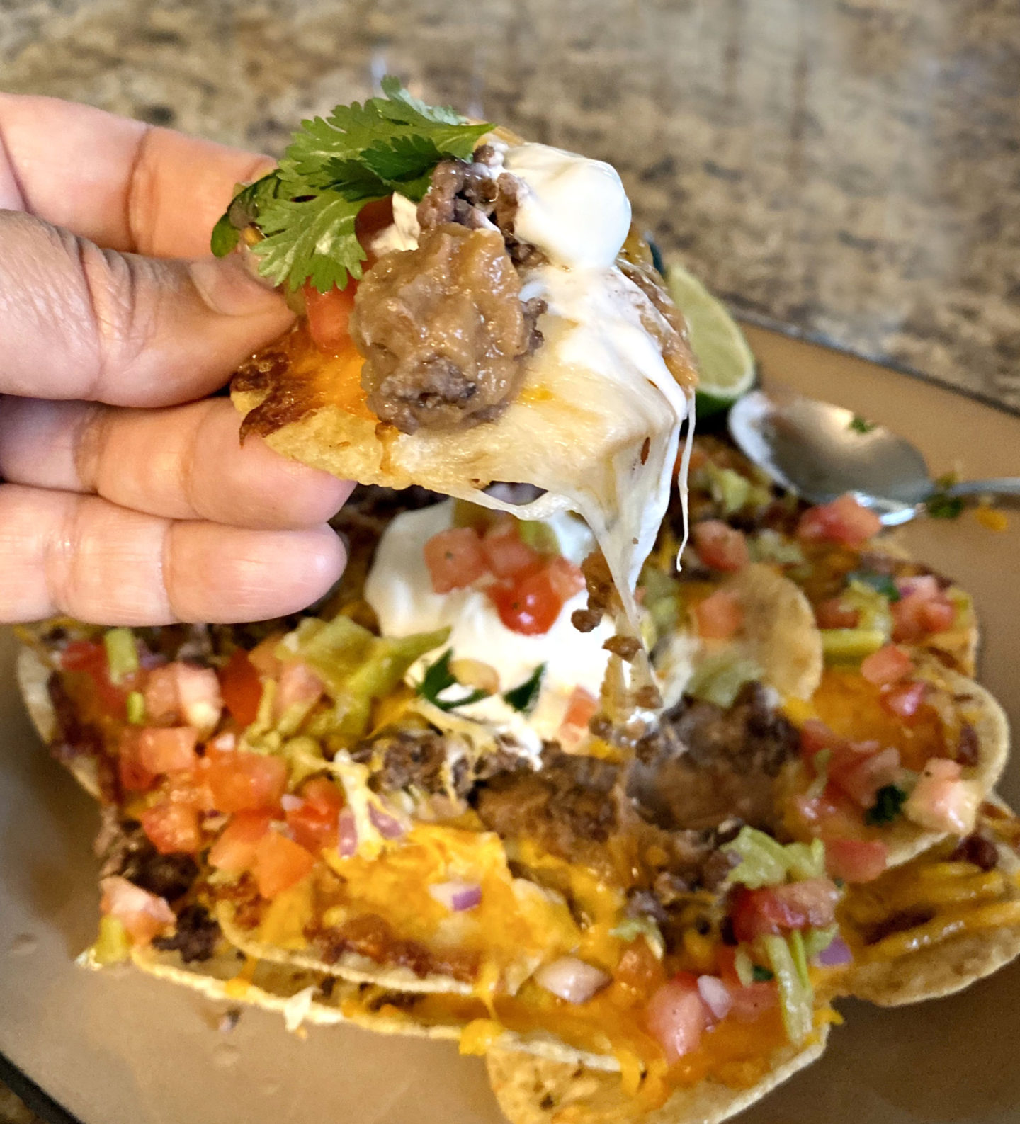 plate of nachos and close up of hand holding a loaded chip
