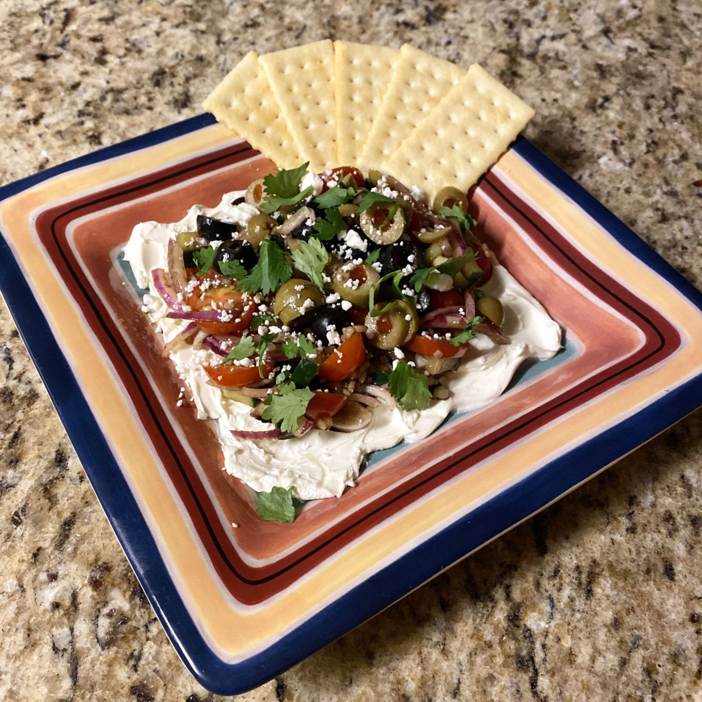 cream cheese and mixed mediterranean veggies and crackers on a plate