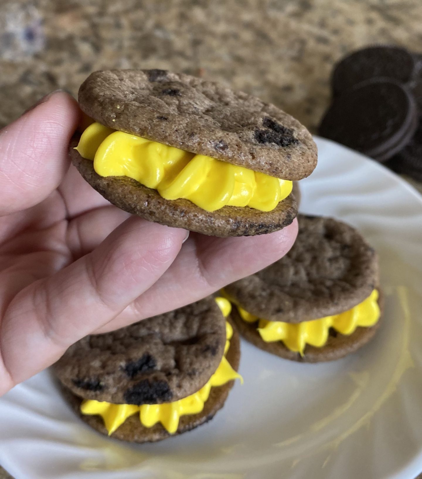 hand holding oreo cookie sandwich with yellow frosting