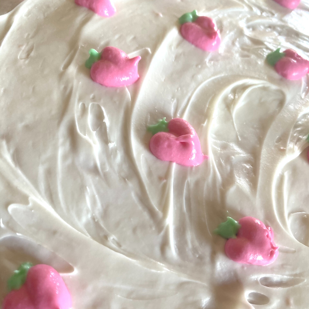 closeup of strawberry cake with buttercream frosting decorated with tiny pink frosting strawberries