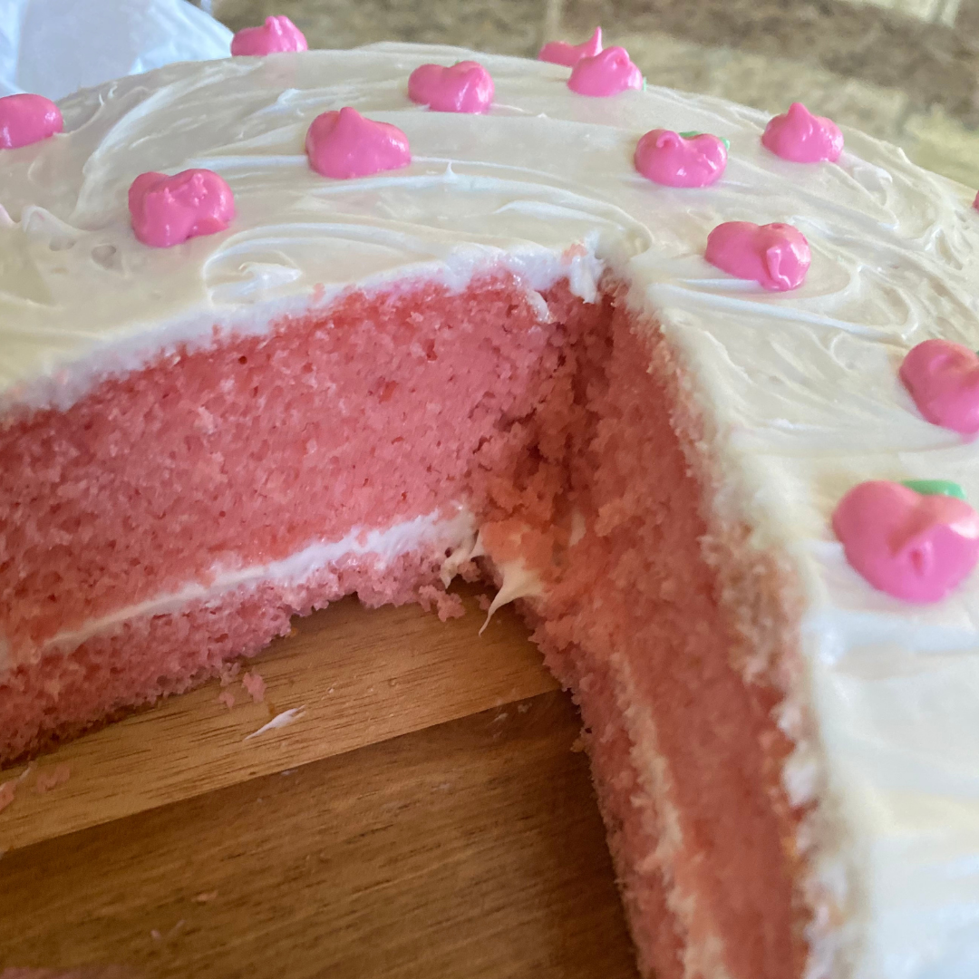 strawberry cake with buttercream frosting and a slice cut out with pink cake inside