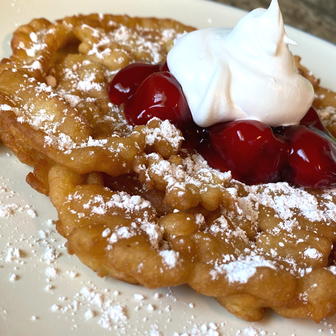 close up of funnel cake with powdered sugar and cherry topping3