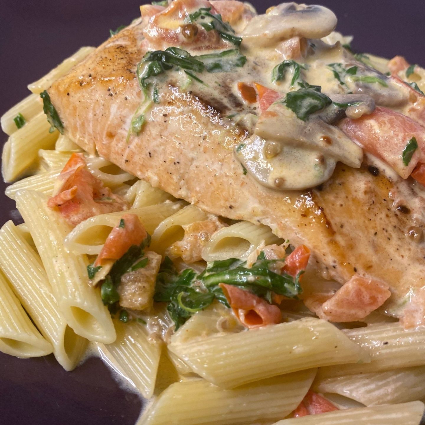 close up of creamy salmon and vegetable medley sauce on penne pasta