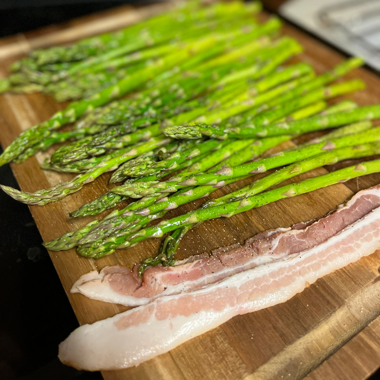 raw asparagus and bacon strips on cutting board