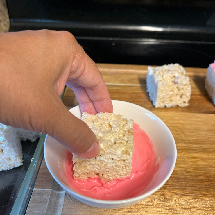 hand dipping rice krispies treats in pink chocolate